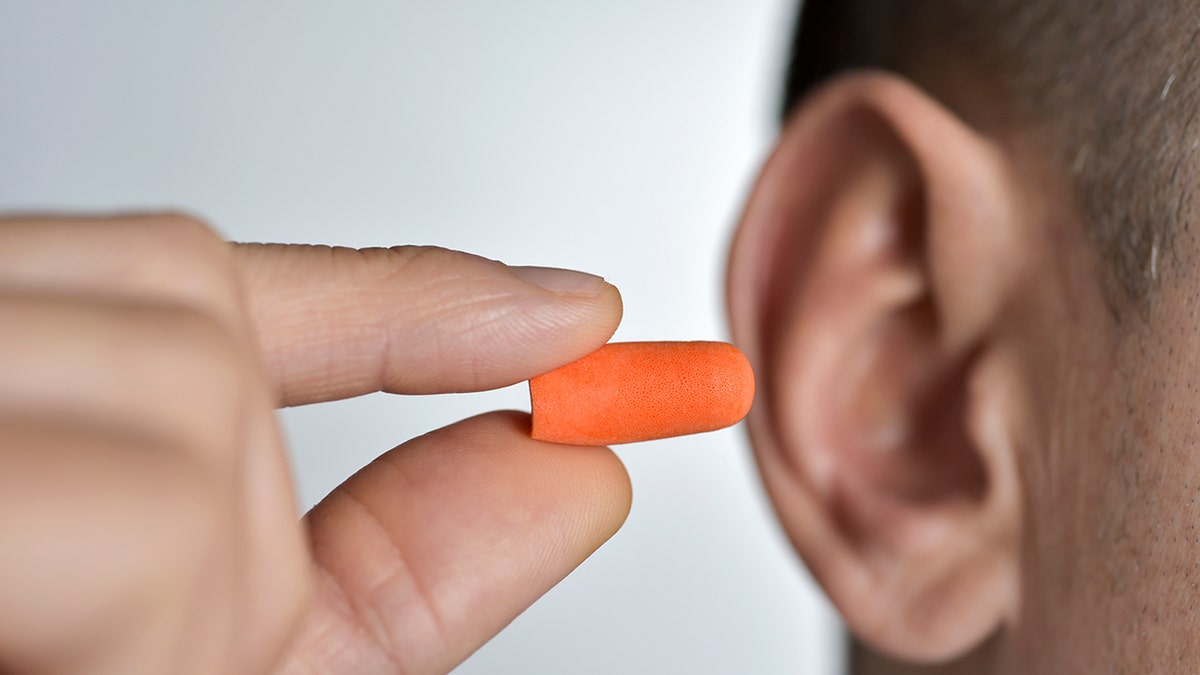 Foreground of a young Caucasian man who inserts an orange counter into his ear